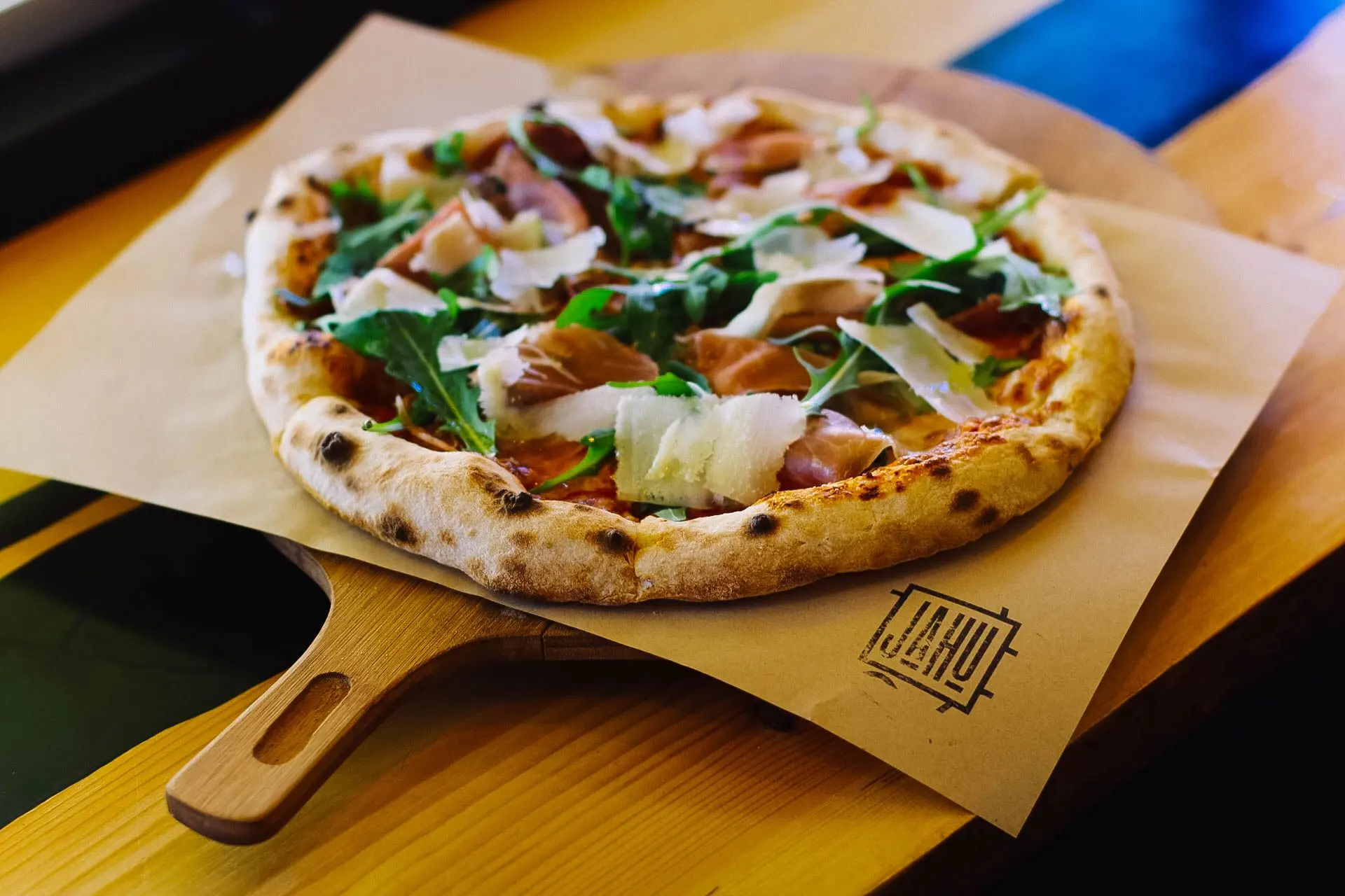 Pizza au jambon de Parme, roquette et copeaux de parmesan, sur une pelle en bois.