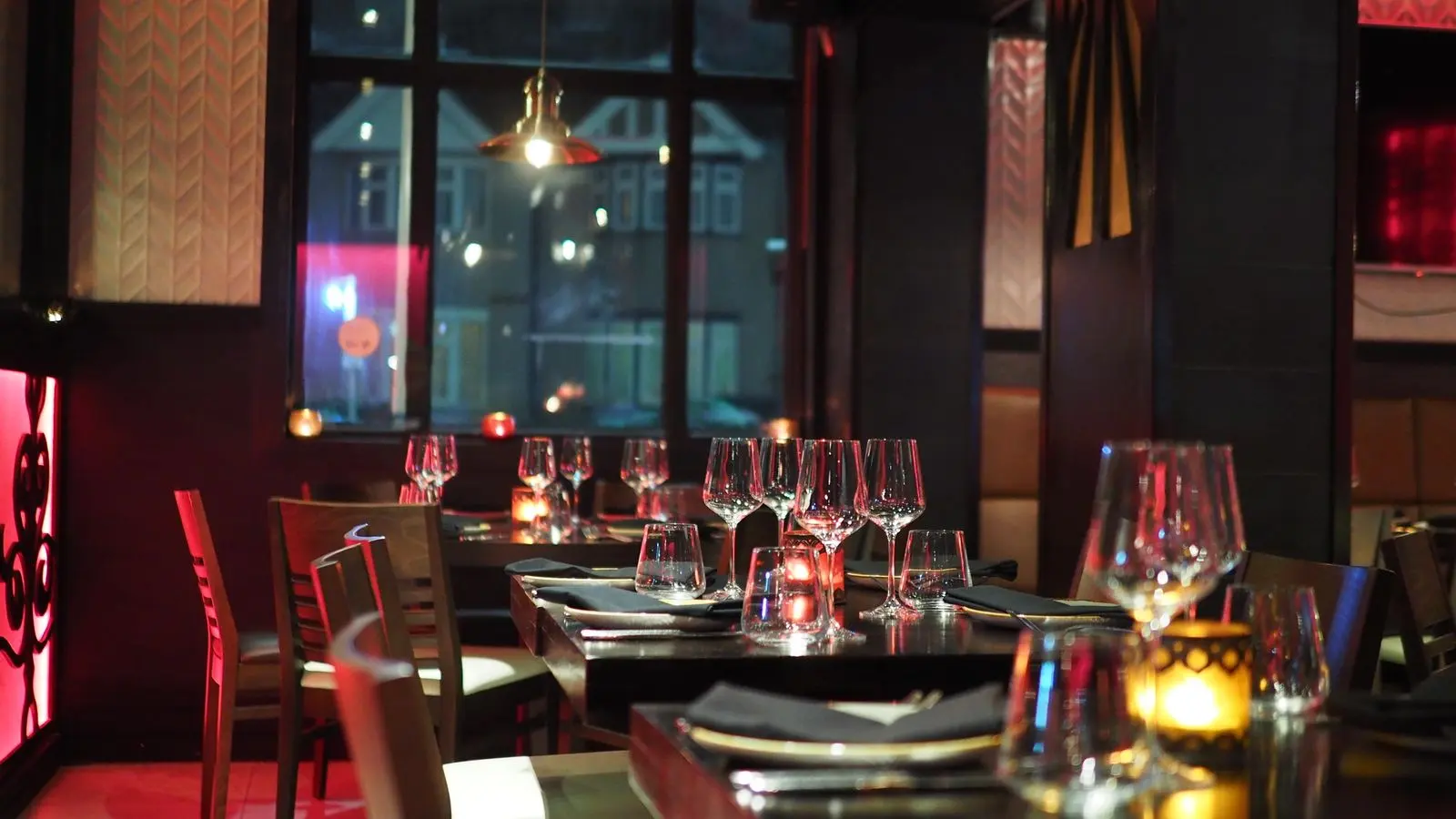 Salle du restaurant à la tombée du soir, tables dressées et bougies allumées.